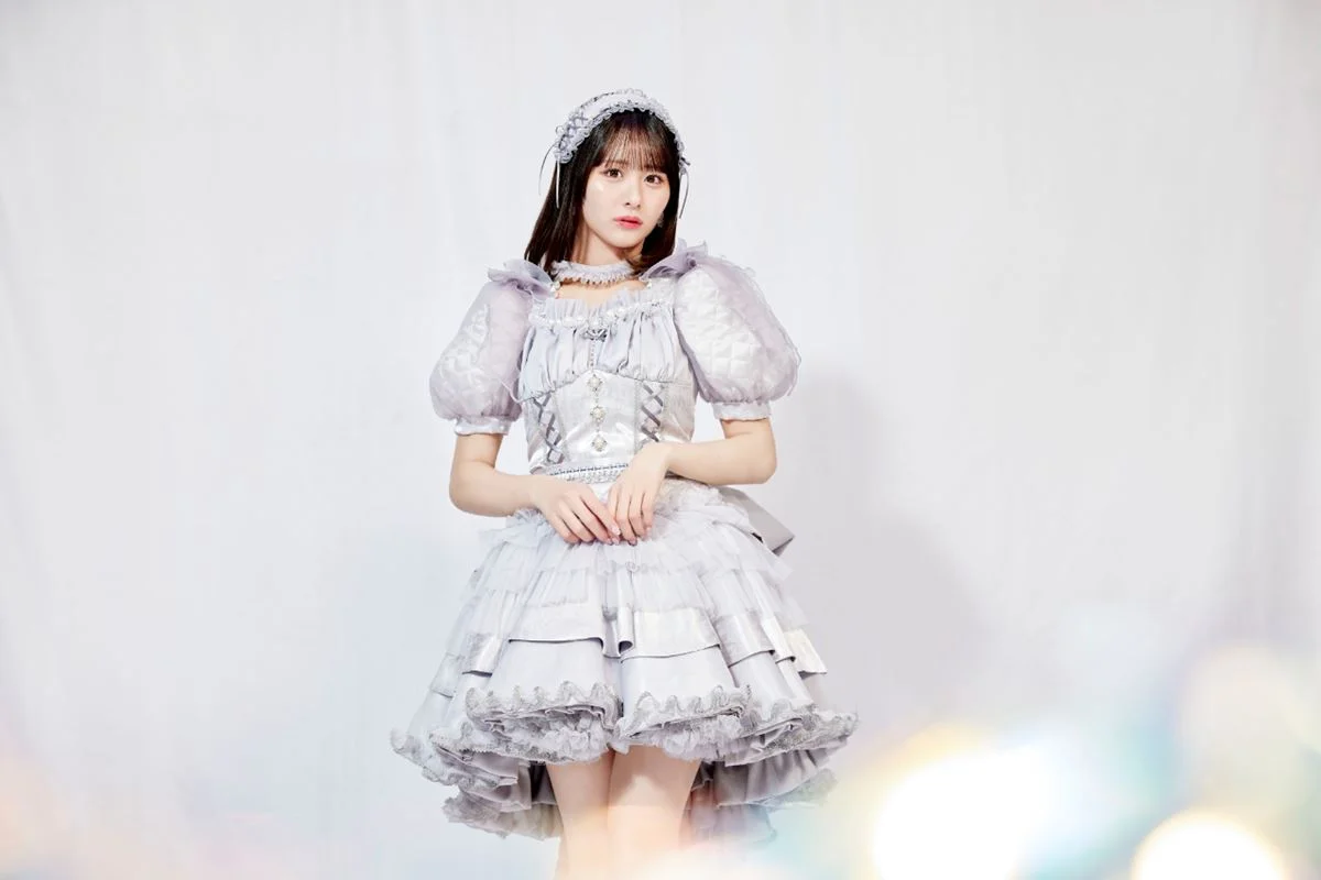 Ảnh nắm tay không có người thứ hai, cô gái trẻ mặc váy lolita trắng đứng trong studio với hai tay đan nhẹ trước bụng