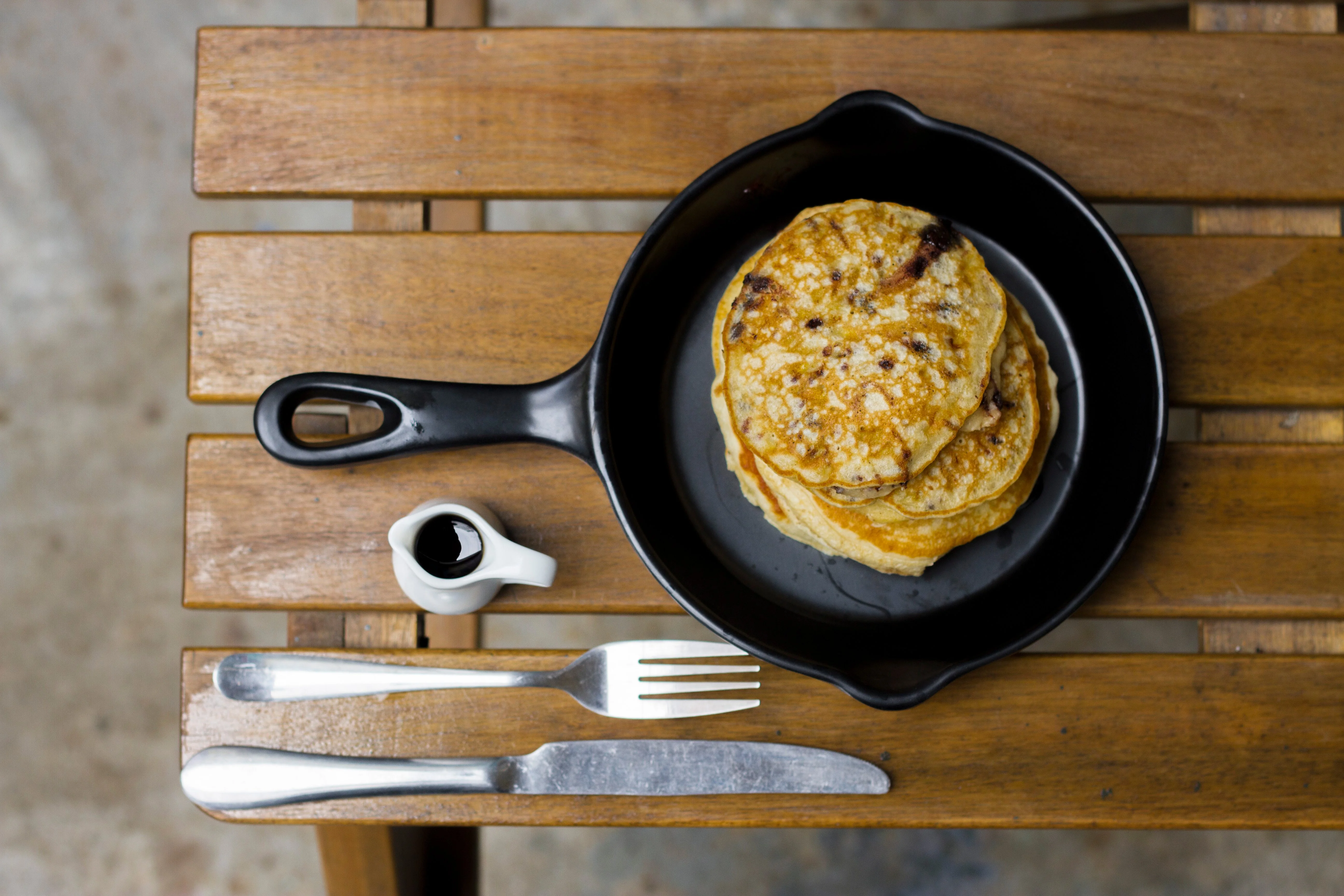 Bánh pancake vàng ruộm trong chảo gang cùng dao nĩa trên bàn gỗ